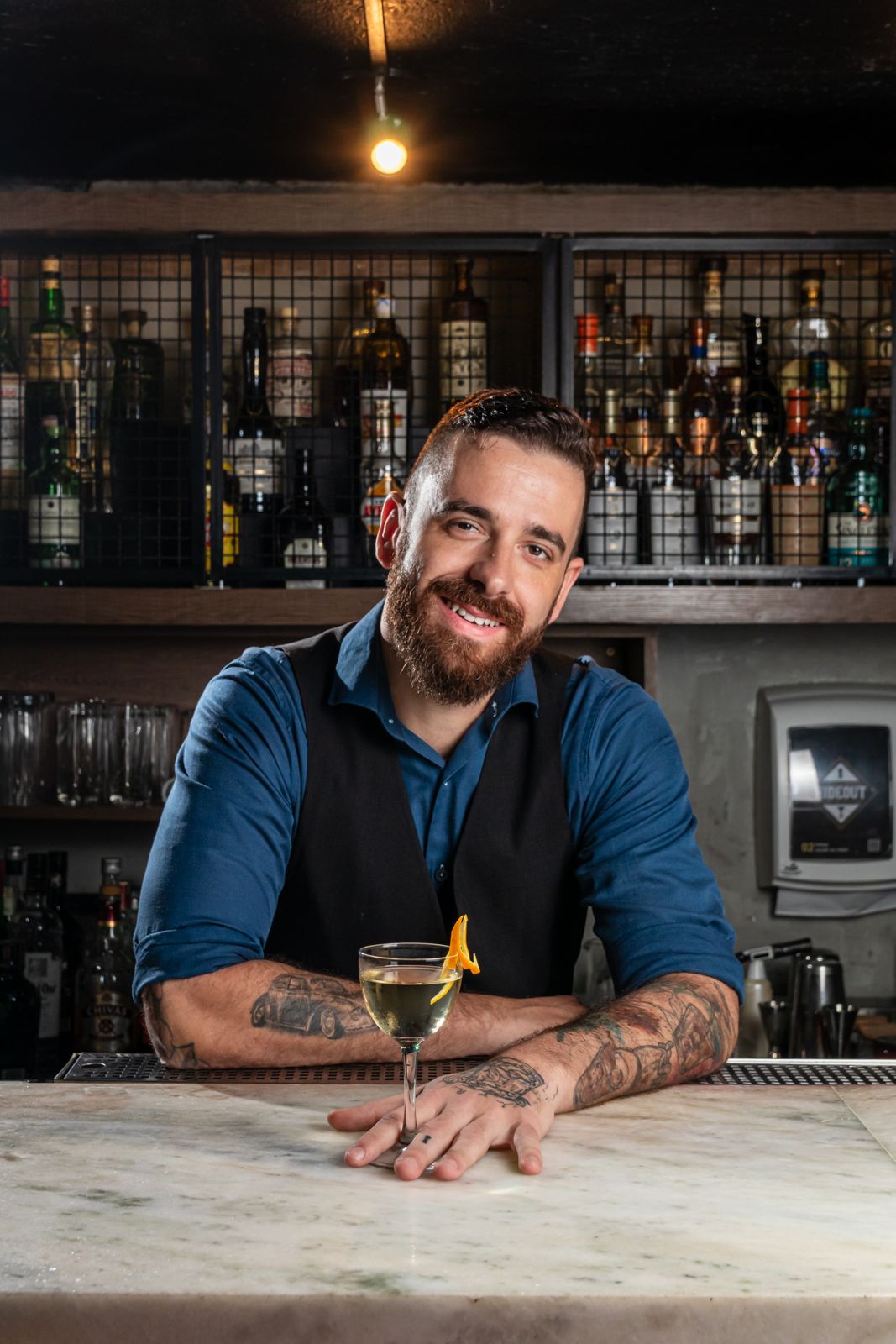 Bartender do Hideout apoiado no balcão de mármore com um coquetel em taça