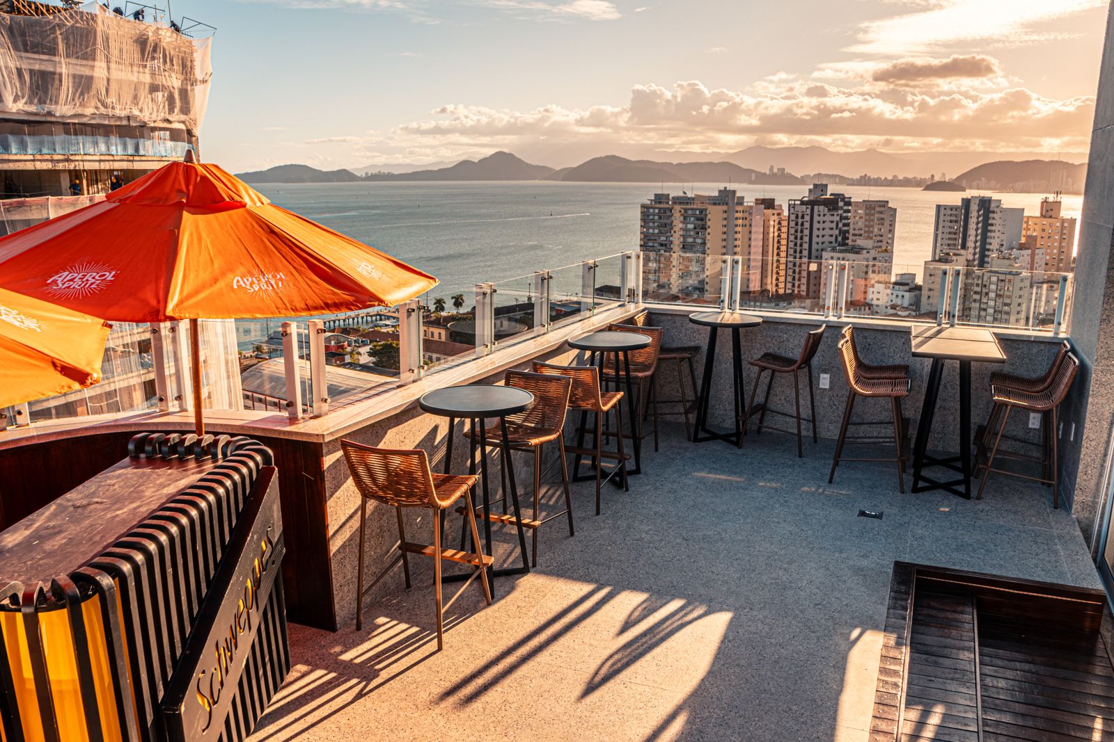 Cobertura do Hideout Fizz ao pôr do sol, com mesas altas e vista para o mar de Santos