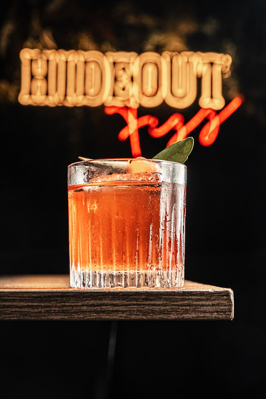 Coquetel em copo baixo diante do letreiro em neon do Hideout Fizz