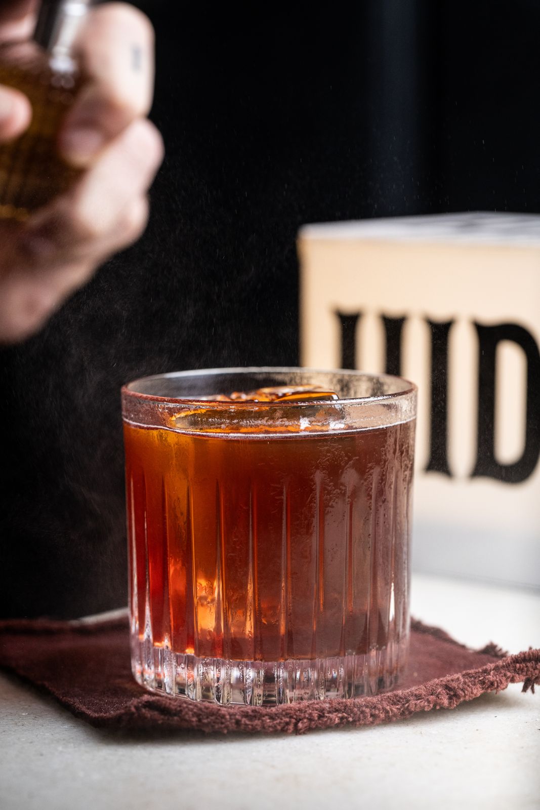 Mão com borrifador sobre um coquetel no Hideout Speakeasy